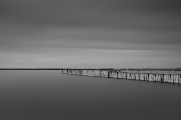 Graustufenaufnahme eines langen Piers in der Nähe des Meeres unter den Gewitterwolken