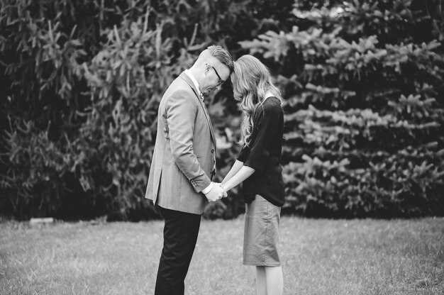 Graustufenaufnahme eines Paares, das die Hände voneinander hält und in einem Garten betet