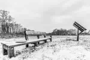 Kostenloses Foto graustufenaufnahme von bänken auf einem schneebedeckten feld unter einem bewölkten himmel