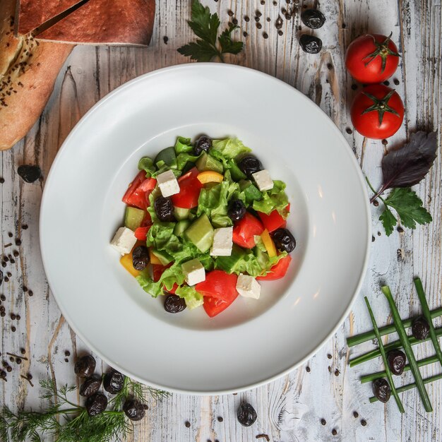 Kostenloses Foto griechischer salat in einem teller mit tomaten, oliven, brot, kräutern und gewürzen