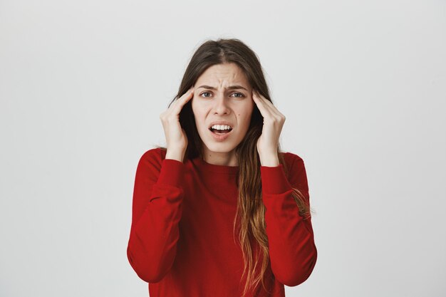 Grimassende Frau, die sich über Kopfschmerzen oder Migräne beschwert