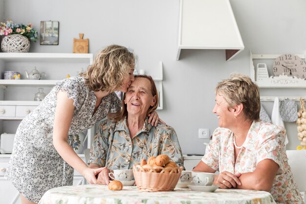 Großartige Tochter, die ihre lächelnde Oma während des Frühstücks küsst