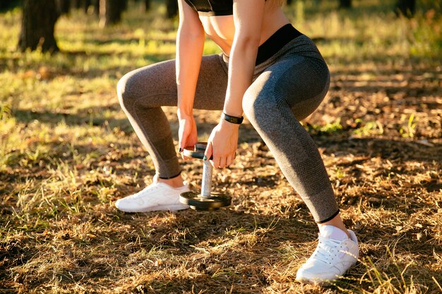 Großaufnahme der Sportfrau, einen Dummkopf anhebend, beim Trainieren im Park.