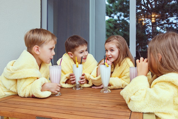 Große Gruppe von Freunden, die sich Zeit für Milchcocktails nehmen. Glücklich lächelnde Jungen und Mädchen in gelben Frotteekleidern. Kindermode-Konzept