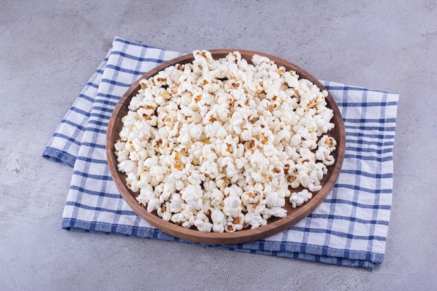 Große Portion knuspriges Popcorn auf einem Holztablett auf einem Handtuch auf Marmorhintergrund. Foto in hoher Qualität