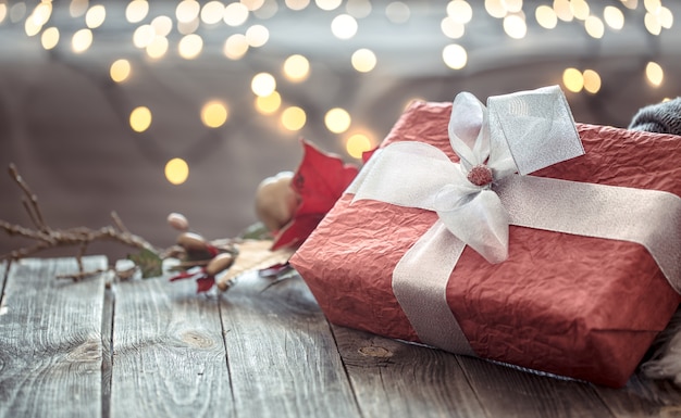 Kostenloses Foto großes rotes geschenk über weihnachtslichtern bokeh im haus auf holztisch mit pullover auf hintergrund und dekorationen. winterstimmung, weihnachtsdekoration, magische weihnachten.