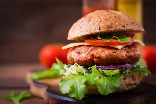 Großes Sandwich - Hamburger mit saftigem Hühnchenburger, Käse, Tomate und roten Zwiebeln auf Holztisch