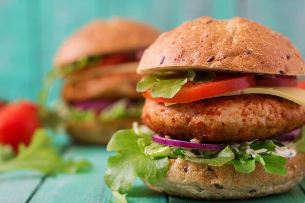 Großes Sandwich - Hamburger mit saftigem Hühnchenburger, Käse, Tomate und roten Zwiebeln auf Holztisch