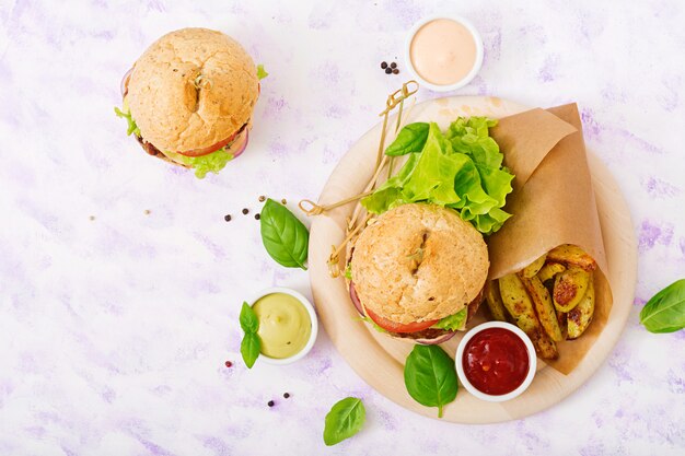 Großes Sandwich - Hamburger mit saftigem Rindfleischburger, Käse, Tomaten, roten Zwiebeln und Pommes Frites. Draufsicht. Flach liegen