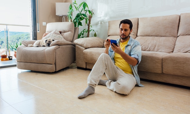 Großformataufnahme eines Mannes, der zu Hause auf dem Boden sitzt und sein Telefon benutzt