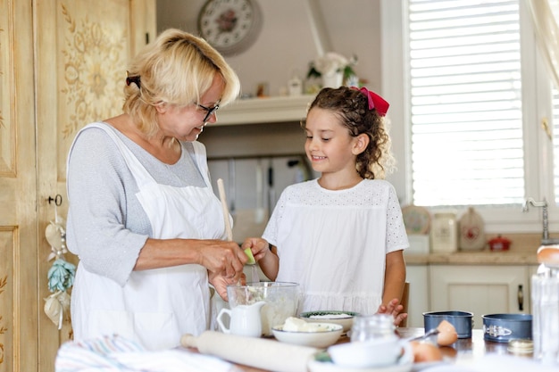 Großmutter und süße kleine lockige enkelin in der küche bereiten zusammen hausgemachte kekse zu. horizontale ansicht. Premium Fotos