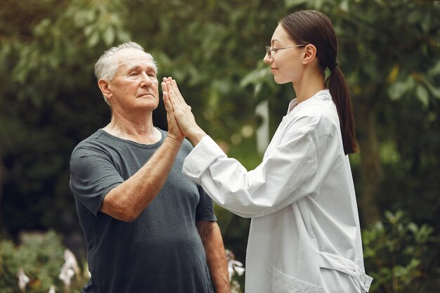 Großvater mit Rollstuhl von Krankenschwester im Freien unterstützt. Älterer Mann und junge Pflegekraft im Park.