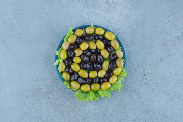 Kostenloses Foto grubenlose oliven auf einer mit salat bedeckten platte auf marmor.