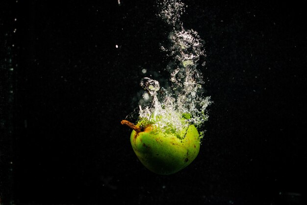 Grüne Birne spritzt Wasser fällt auf schwarzem Hintergrund