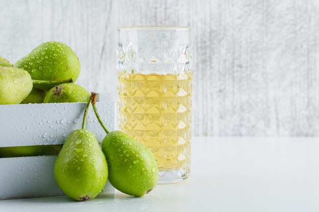 Grüne Birnen mit Getränk in einer Holzkiste auf weißem und schmuddeligem Hintergrund, Seitenansicht.