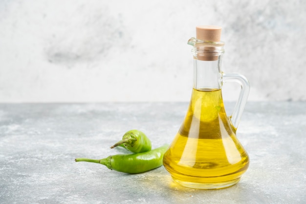 Grüne Chilischoten mit einer Flasche nativem Olivenöl extra auf Marmortisch.