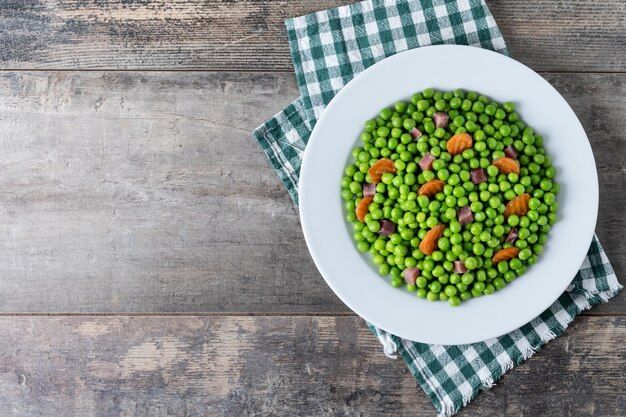 Grüne Erbsen mit Serrano-Schinken und Karotten auf Holztisch