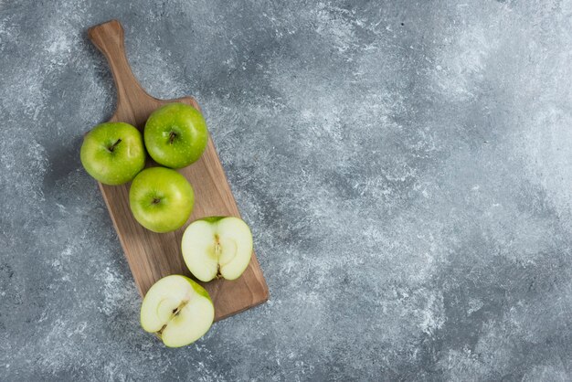 Grüne ganze und geschnittene Äpfel auf Holzbrett.