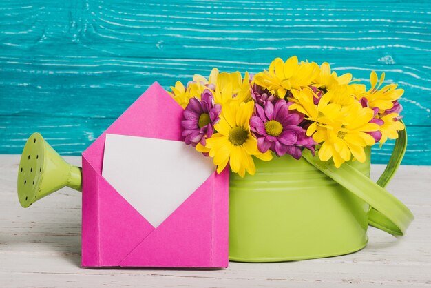 Grüne Gießkanne mit Blumen und rosa Umschlag