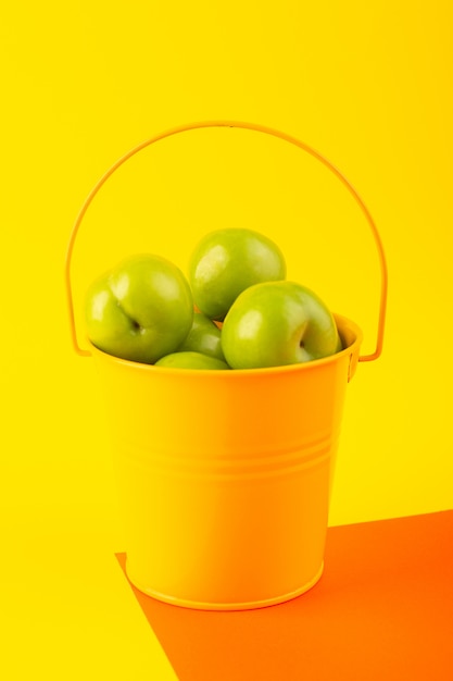 Grüne Kirschpflaume der Draufsicht innerhalb des gelben Korbs auf der sauren Zusammensetzung des orange und gelben Hintergrundfruchts