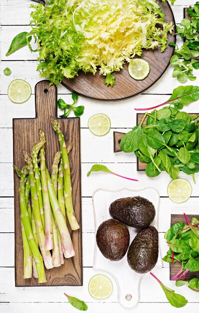 Grüne Kräuter, Spargel und schwarze Avocado auf einem weißen hölzernen Hintergrund. Ansicht von oben. Flach liegen