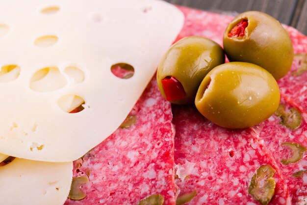 Grüne Oliven liegen auf geschnittenem Schweizer Käse und Salami