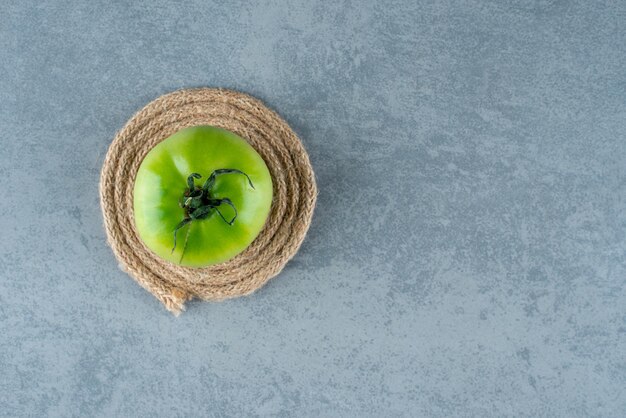 Grüne Tomate mit Seil auf Marmor.