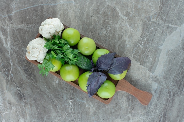 Grüne Tomaten und Blumenkohlstücke mit Amaranth- und Petersilienblättern auf einem Tablett auf Marmor.