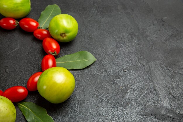 Grüne Tomaten und Lorbeerblätter der Kirsche Tomaten der unteren Nahansicht auf dunklem Hintergrund