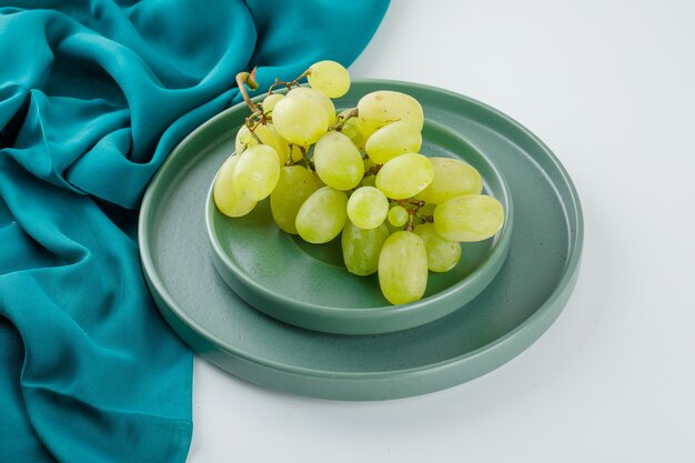 Grüne Trauben in einer Untertasse mit Plattenhochwinkelansicht auf Weiß und Textil