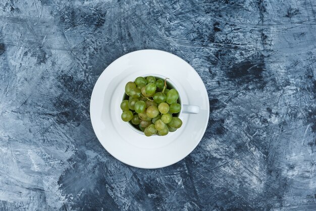 Grüne Trauben in einer weißen Tasse mit Plattenoberansicht auf einem grungy Gipshintergrund