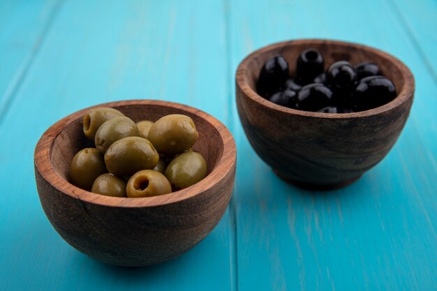 Grüne und schwarze Oliven der Vorderansicht in Schalen auf türkisfarbenem Hintergrund