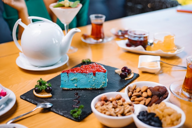 Grüner Minzkäsekuchen der Seitenansicht auf einer schwarzen Bordüre, die mit Tee auf dem Tisch serviert wird