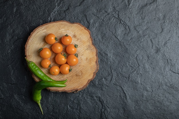 Grüner paprika und kirschtomaten auf dem holzstück mit schwarzem hintergrund. hochwertiges foto