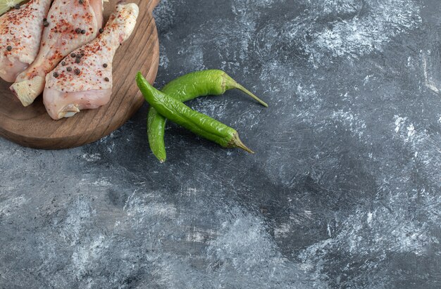 Grüner Pfeffer mit Hähnchenschenkeln über grauem Hintergrund.