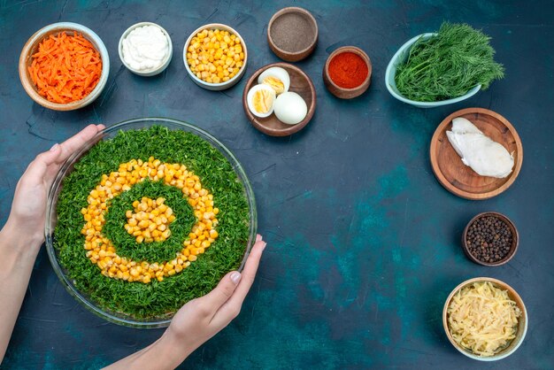 Grüner Salat der Draufsicht mit Körnern zusammen mit geschnittenen Karotten und Eiern auf dem dunkelblauen Schreibtisch.