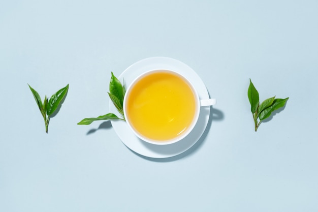 Grüner Tee in Tasse mit Teeblättern auf blauem Pastellhintergrund gebraut. Draufsicht.