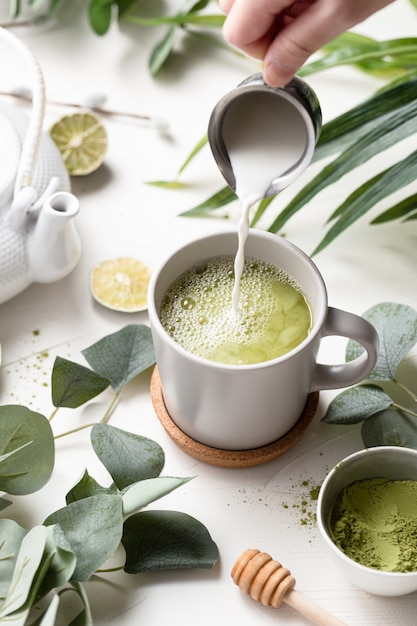 Grüner Tee Latte mit Milch in einer weißen Tasse mit grünen Blättern und Holzlöffel