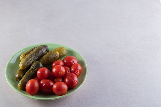 Grüner Teller mit eingelegten Gurken und Tomaten auf Steintisch.