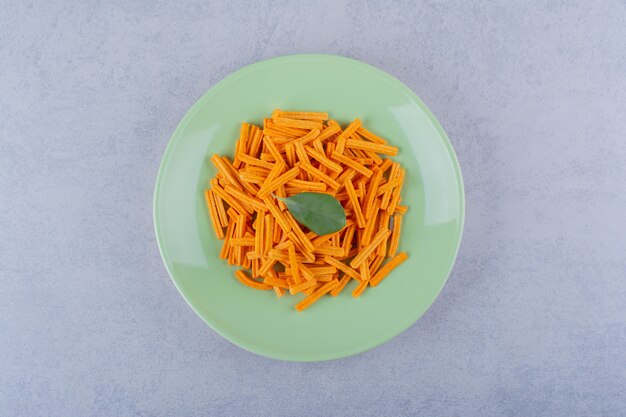 Grüner Teller mit knusprigen Kartoffelchips auf Steintisch.