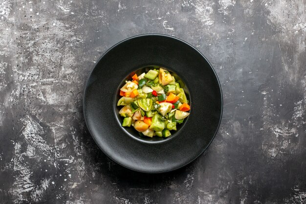 Grüner Tomatensalat der Draufsicht auf schwarzem ovalem Teller auf dunklem Hintergrund