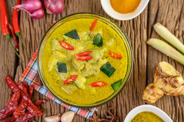 Grünes Curry in einer Schüssel und Gewürzen auf Holztisch.