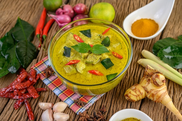 Grünes Curry in einer Schüssel und Gewürzen auf Holztisch.