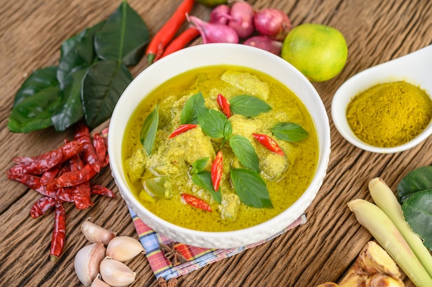 Grünes Curry in einer Schüssel und Gewürzen auf Holztisch.