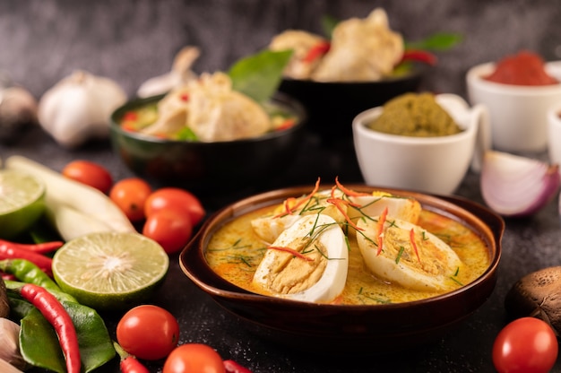 Grünes Curry mit Eiern in schwarzen Tassen, mit Zitrone, Zitronengras, Chili und Tomaten.