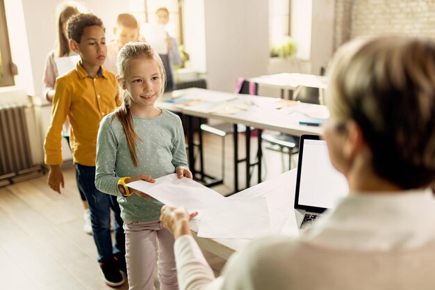 Grundschüler, die ihre Testergebnisse von einem Lehrer im Klassenzimmer entgegennehmen