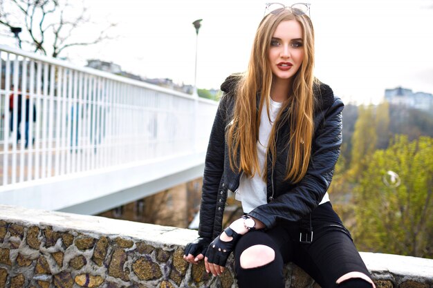 Grunge Mode Porträt der stilvollen blonden Frau, Leder Bikerjacke und Handschuhe, Rock'n'Roll Stimmung, Stadtansicht auf Stadtbrücke, Straßenmode, Frisur Make-up, Reisender.