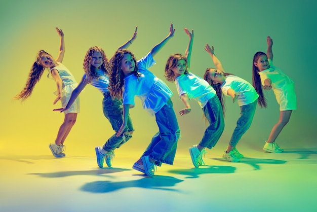 Gruppe aktiver Kinder, fröhliche Mädchen tanzen einzeln auf grünem Hintergrund in Neonlicht