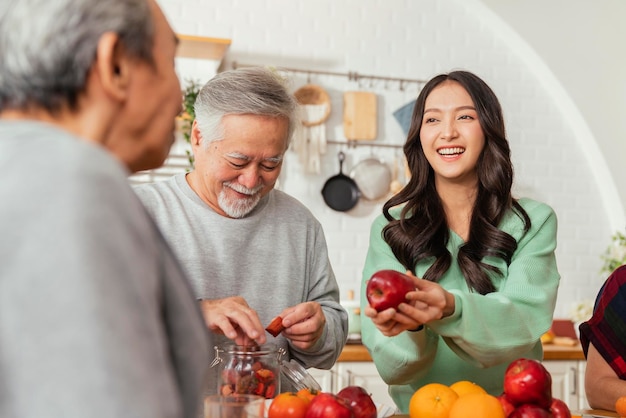 Gruppe asiatischer älterer älterer Freunde bei Dinnerparty zu Hause Ältere Freundin bereitet mit ihrer Tochter Salat und Fruchtsaft zu mit lächelndem fröhlichem Moment Gespräch mit älterem Freund lachen Lächeln