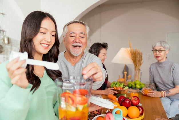 Gruppe asiatischer älterer älterer Freunde bei Dinnerparty zu Hause Ältere Freundin bereitet mit ihrer Tochter Salat und Fruchtsaft zu mit lächelndem fröhlichem Moment Gespräch mit älterem Freund lachen Lächeln